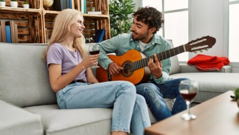 Man playing an acoustic guitar to a woman holding a wine glass.