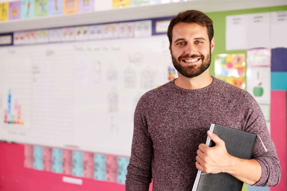 Smiling male teacher standing in front of his whiteboard