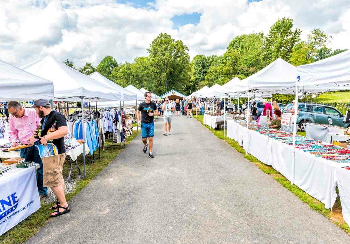 A sidewalk lined with booths selling goods and people shopping in the sun.