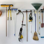 Common gardening tools, including a rake, shovel, chainsaw, and weed whacker, hang on a rack.